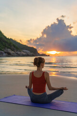 Fototapeta na wymiar Woman practices yoga. Woman sitting in lotus position and meditating at sunrise on the beach
