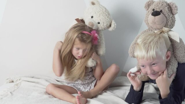 Children boy and little girl jump on bed with teddy bears