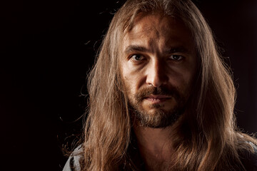 Long-haired masculine middle-aged man standing in the dark