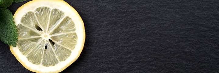 Panoramic image of sliced yellow lemon with leaves of fresh lemon balm (Melissa officinalis) on...