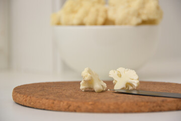 A cauliflower piece split in half on a wooden surface with cauliflower in a white bowl in the background.