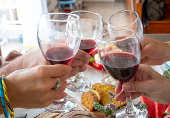 Four people toasting with red wine glasses over the table ready with food. Party and togetherness concept