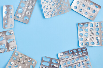 frame empty blister packs of pills with one partially full pack on blue background. flat lay, copy space