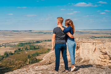 Rear view of a romantic couple a man and a woman standing on the edge of a cliff on a White rock in Crimea with a view of the rural landscape