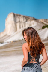 Rear view of a brunette woman in a dress standing against a White rock in Crimea