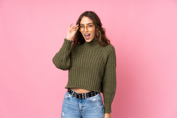 Young woman over isolated pink background with glasses and surprised