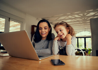 Cheerful woman with preschool daughter watching funny videos on laptop at home