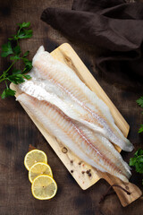 Cod fillet. Raw cod fillet on a chopping board on a brown kitchen table. Preparation for cooking fish. Top view	