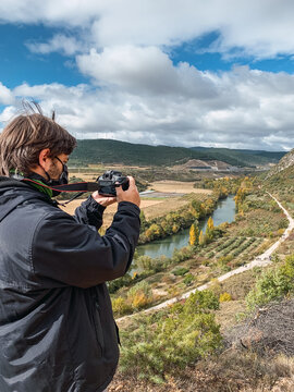 Young man taking photos from a hill of a river and trees on a valley