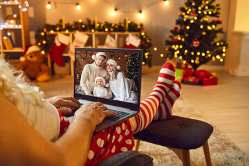 Relaxed Santa with laptop having online video call with happy family on Christmas Day