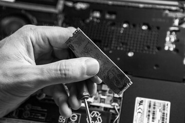 The service technician holds a new ssd drive in his hands, which he wants to put in the laptop, and he hopes that after that it will work. Black and White.