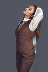 Fashion minimalist portrait of brunette female model on grey background. stylish clothing with scottish color, casual suit with women akcent  white silk shirt - obrazy, fototapety, plakaty