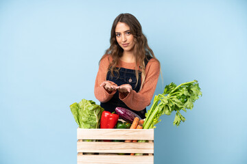 Farmer with freshly picked vegetables in a box holding copyspace imaginary on the palm to insert an...