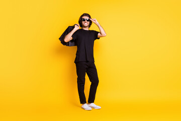 Fototapeta na wymiar Full length photo of young man hold shopping packages glasses wear black t-shirt pants white sneakers sunglass isolated yellow color background