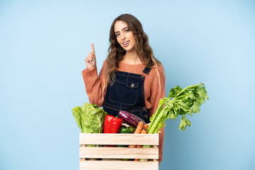 Farmer with freshly picked vegetables in a box showing and lifting a finger in sign of the best