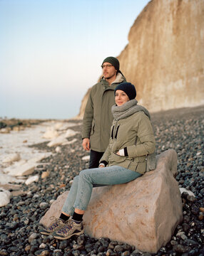 couple sur une plage de galets regardant l'horizon au coucher du soleil