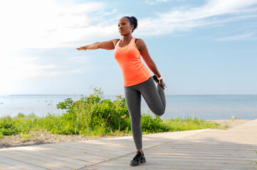 fitness, sport and healthy lifestyle concept - young african american woman exercising on beach
