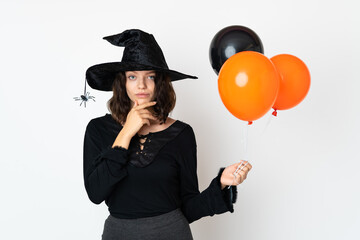 Young witch holding black and orange air balloons thinking