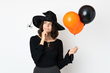 Young witch holding black and orange air balloons having doubts and thinking