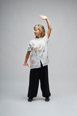 Mature blonde woman practicing Chi kung and Tai Chi on a white background. She wears a traditional white chinese Tai Chi jacket, black trousers and black shoes with ying yang symbol
