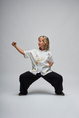 Mature blonde woman practicing Chi kung and Tai Chi on a white background. She wears a traditional white chinese Tai Chi jacket, black trousers and black shoes with ying yang symbol