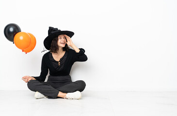 Young witch holding black and orange air balloons sitting on the floor smiling a lot