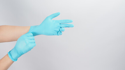 Hand is pulling blue latex gloves on white background.