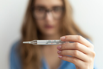 Medical thermometer showing high temperature close-up being held by young blonde woman.