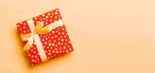 wrapped Christmas or other holiday handmade present in paper with Gold ribbon on orange background. Present box, decoration of gift on colored table, top view with copy space