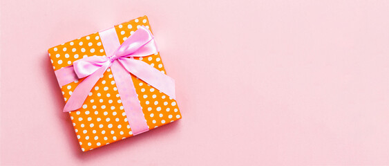 Obraz premium wrapped Christmas or other holiday handmade present in paper with pink ribbon on pink background. Present box, decoration of gift on colored table, top view with copy space