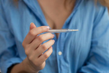 Woman checking body temperature with medical thermometer close-up.