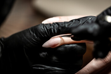 Manicurist is applying electric nail file drill to manicure on female fingers. Woman getting nail...