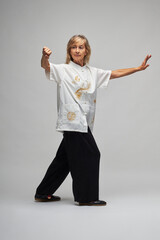 Mature blonde woman practicing Chi kung and Tai Chi on a white background. She wears a traditional white chinese Tai Chi jacket, black trousers and black shoes with ying yang symbol