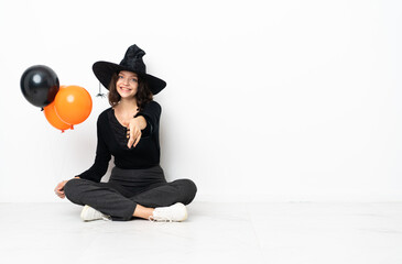 Young witch holding black and orange air balloons sitting on the floor shaking hands for closing a good deal