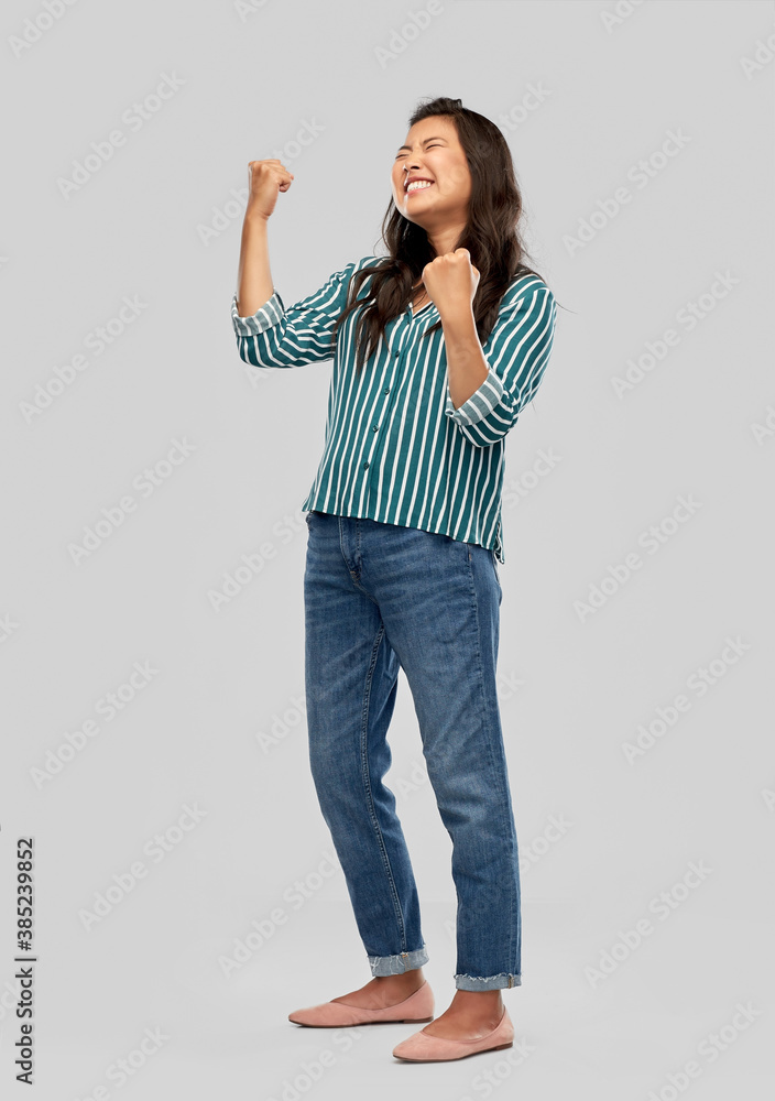 Wall mural success, winning gesture and people concept - happy young asian woman celebrating victory over grey 