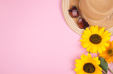 Flatlay with sunglasses, straw hat and bright yellow sunflower on pink background.