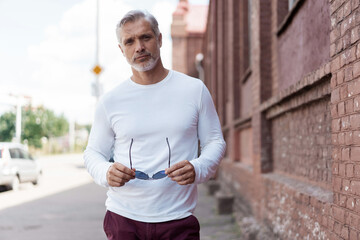 Obraz premium Portrait of a Grey-haired Mature handsome man in jeans and white t-shirt leaning to the old wall.
