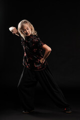 Mature blonde woman practicing Tai Chin Chen style in a black background wearing a traticional chinese black jacket with red decoration, black trousers and traditional shoes with ying yang symbol