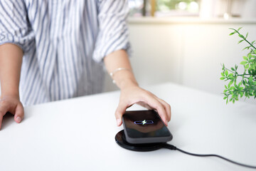 Charging mobile phone battery with wireless charging device in the table. Smartphone charging on a...