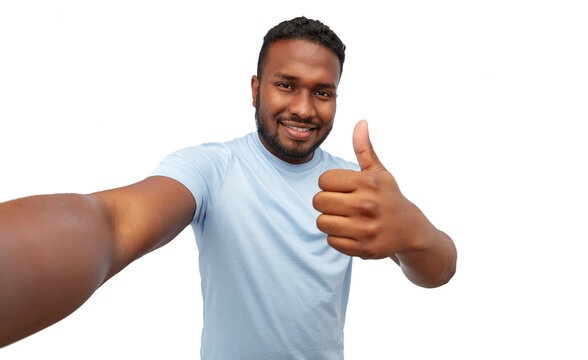 people, grooming and beauty concept - portrait of happy smiling young african american man taking selfie showing thumbs up over white background