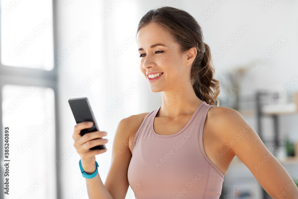 Wall mural sport, fitness and technology concept - happy smiling young woman with smatphone exercising at home