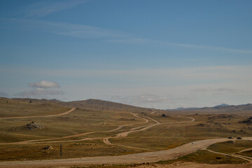 Winding roads in steppe among hills and mountains covered with green yellow grass. Baikal nature. Mountain ranges.