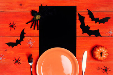 Halloween table setting with plate, cutlery and spooky decorations on orange wooden table.