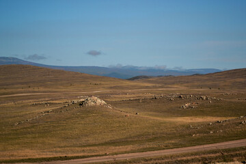 Road in steppe among stones hills and mountains covered with green yellow grass. Baikal nature. Mountain ranges. Trees