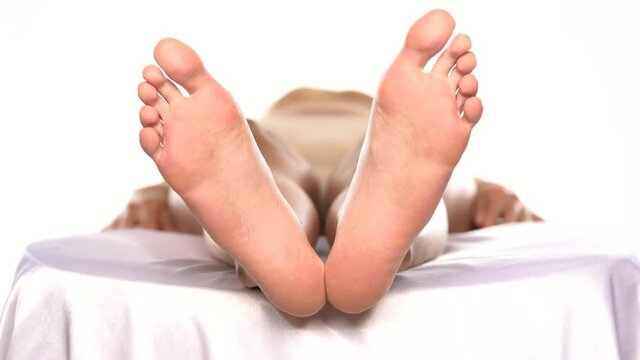 a woman lying on the bed and slowly moving her bare feet on a white background
