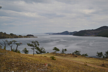 Autumn view of bay of Lake Baikal with islands and peninsulas and mountains on horizon. Ripples on water, green trees, clouds in sky