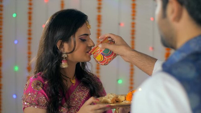 Newly-wed Indian couple happily performing Karwa Chauth rituals together. Over the shoulder shot of an Indian husband feeding water to his beautiful wife - Indian customs 