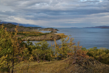 Autumn view of bay of Lake Baikal with islands and peninsulas and mountains on horizon. Blue water, red and green trees