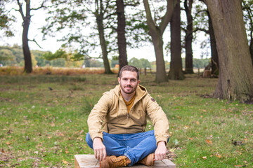 Naklejka na ściany i meble Photo of a young and attractive man sitting on a tree trunk practising meditation in the middle of nature. Self isolation in a forest. Relax