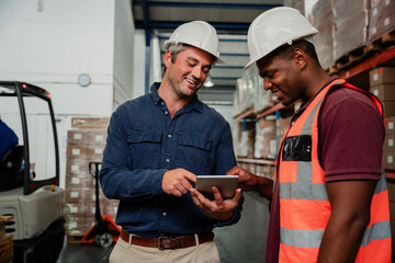 Business banker and factory worker colleagues at work holding digital tablet searching for packages